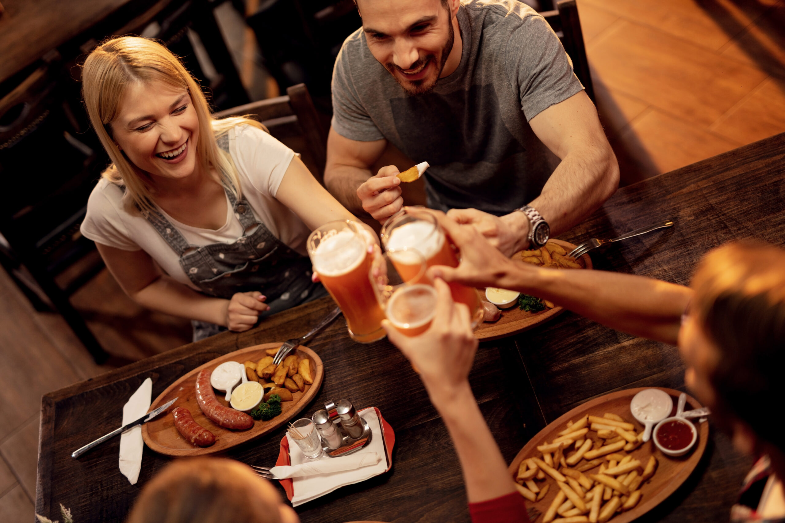 Happy friends celebrating and toasting with beer during lunch in a pub.